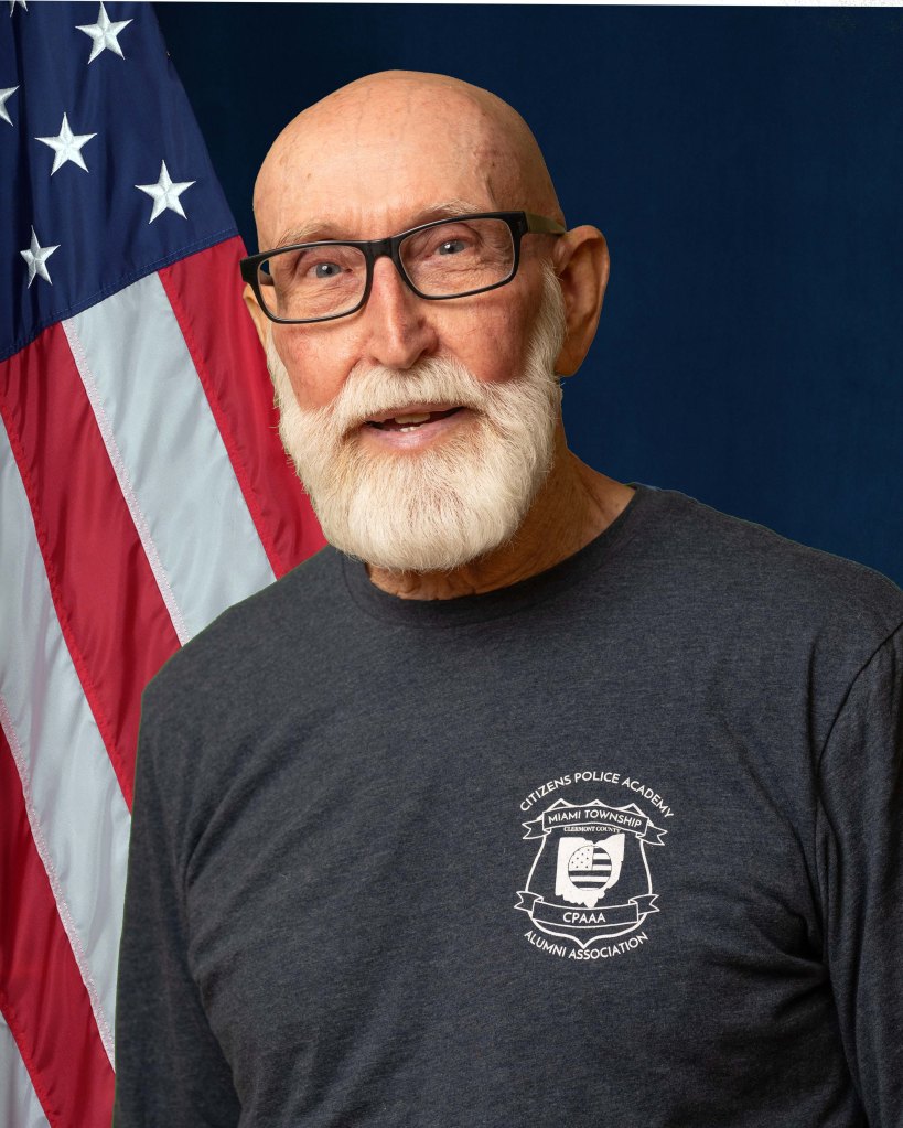 A portrait of Rodger Earnest in front of an American Flag and blue background.