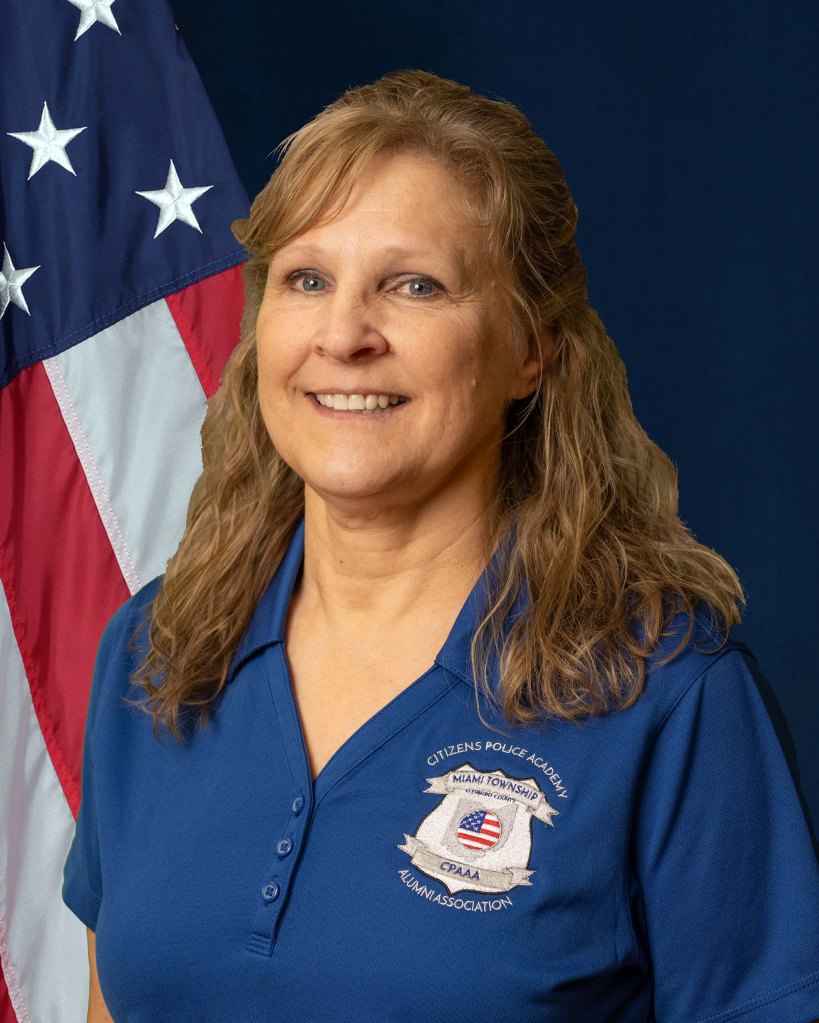 A portrait of Trish Day in front of an American Flag and blue background.